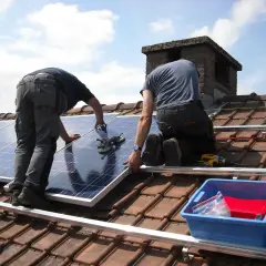 Montaż paneli fotowoltaicznych na dachu. Dwóch pracowników instaluje panele, jeden przytrzymuje, drugi dokręca.