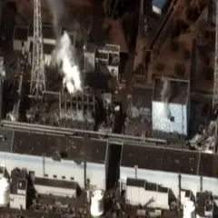 Widok z lotu ptaka na zniszczoną elektrownię Fukushima. Widać dym wydobywający się z uszkodzonych budynków, świadectwo katastrofy.
