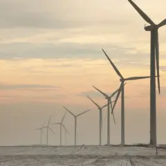 Rząd potężnych farm wiatrowych na tle zachodzącego słońca, tworzący malowniczy krajobraz.
