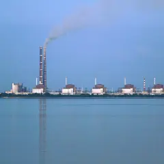 Zaporoże: potężna elektrownia atomowa z chłodnią kominową i dymiącymi kominami, na tle spokojnej wody.