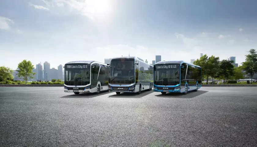 Trzy nowoczesne autobusy elektryczne MAN Lion's City E stoją na tle miejskiej panoramy.