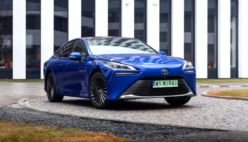 Niebieski samochód na wodór, Toyota Mirai, parkuje przed nowoczesnym budynkiem.