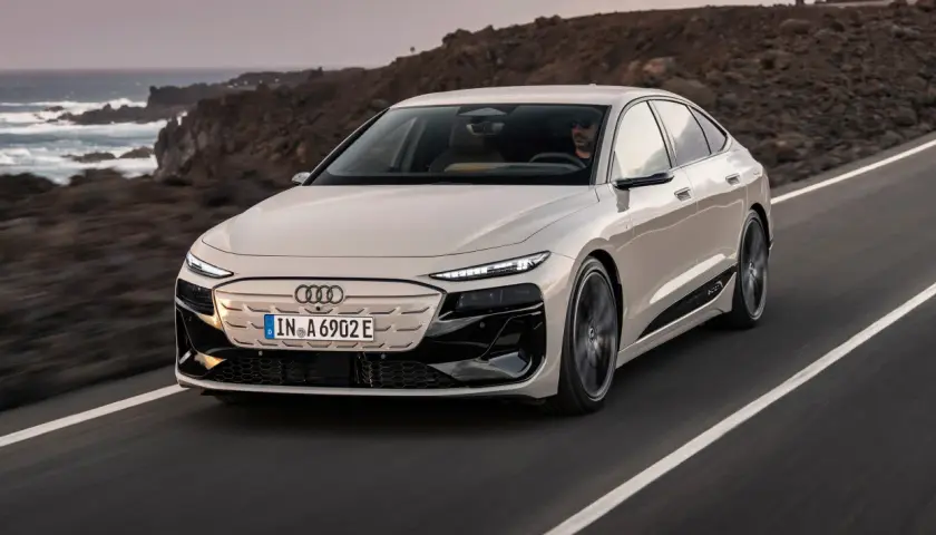 Elegancki Audi A6 e-tron w kolorze kremowym przemierza malowniczą, nadmorską drogę.
