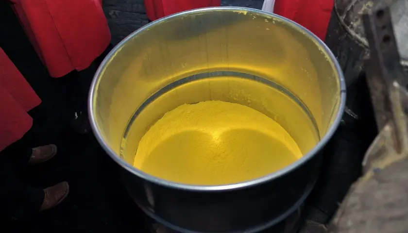Żółty proszek, być może uran, w metalowym pojemniku. Wokół widać fragmenty czerwonych fartuchów.