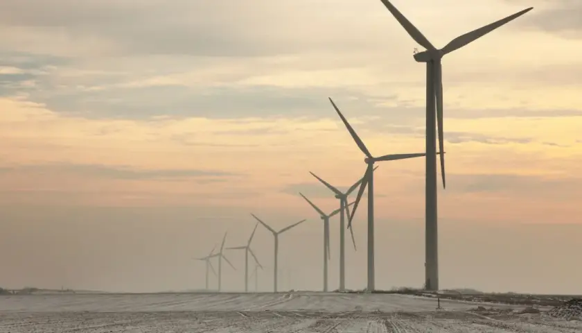 Rząd potężnych farm wiatrowych na tle zachodzącego słońca, tworzący malowniczy krajobraz.