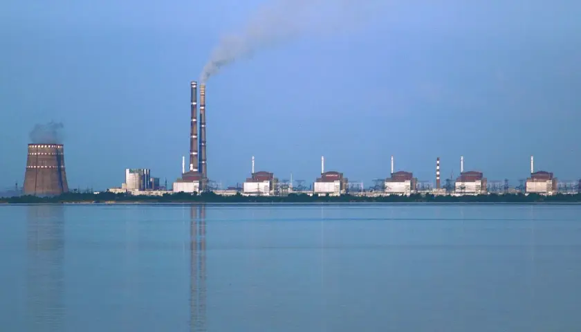 Zaporoże: potężna elektrownia atomowa z chłodnią kominową i dymiącymi kominami, na tle spokojnej wody.
