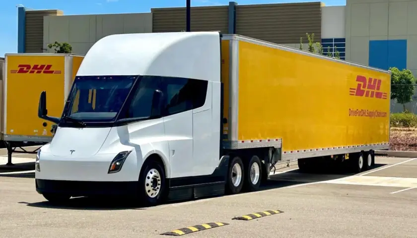 Biała ciężarówka Tesla Semi z żółtą naczepą DHL stoi na parkingu.
