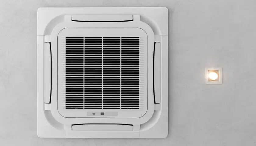 Kasetowa klimatyzacja zamontowana na suficie, obok kwadratowej lampy.